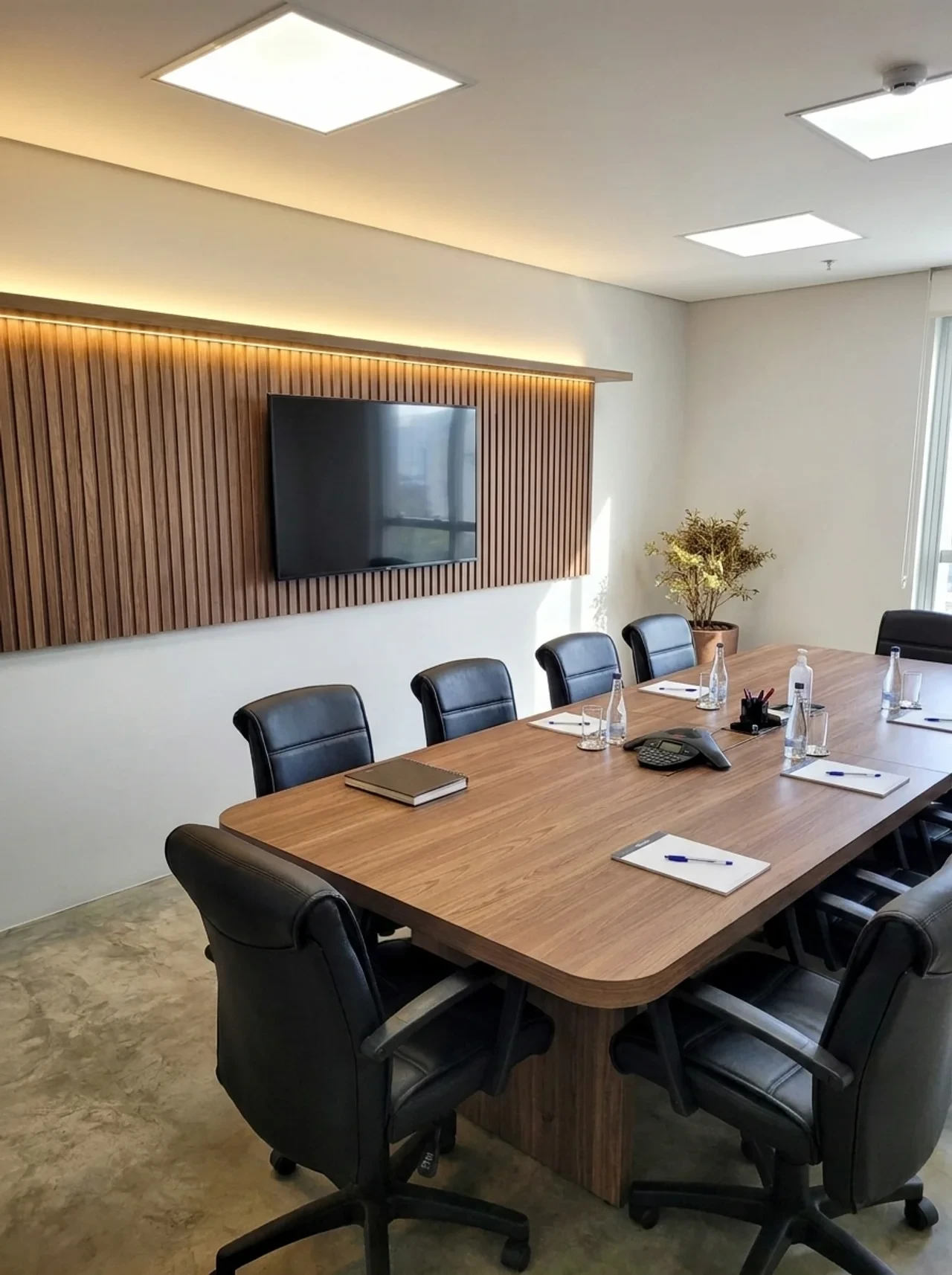 Sala de reunião com painel ripado em madeira, TV e iluminação embutida