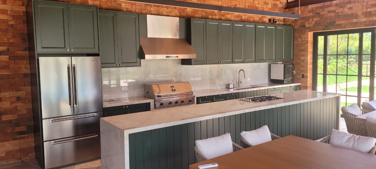 Cozinha gourmet em verde com ilha em mármore, churrasqueira e tijolinho à vista