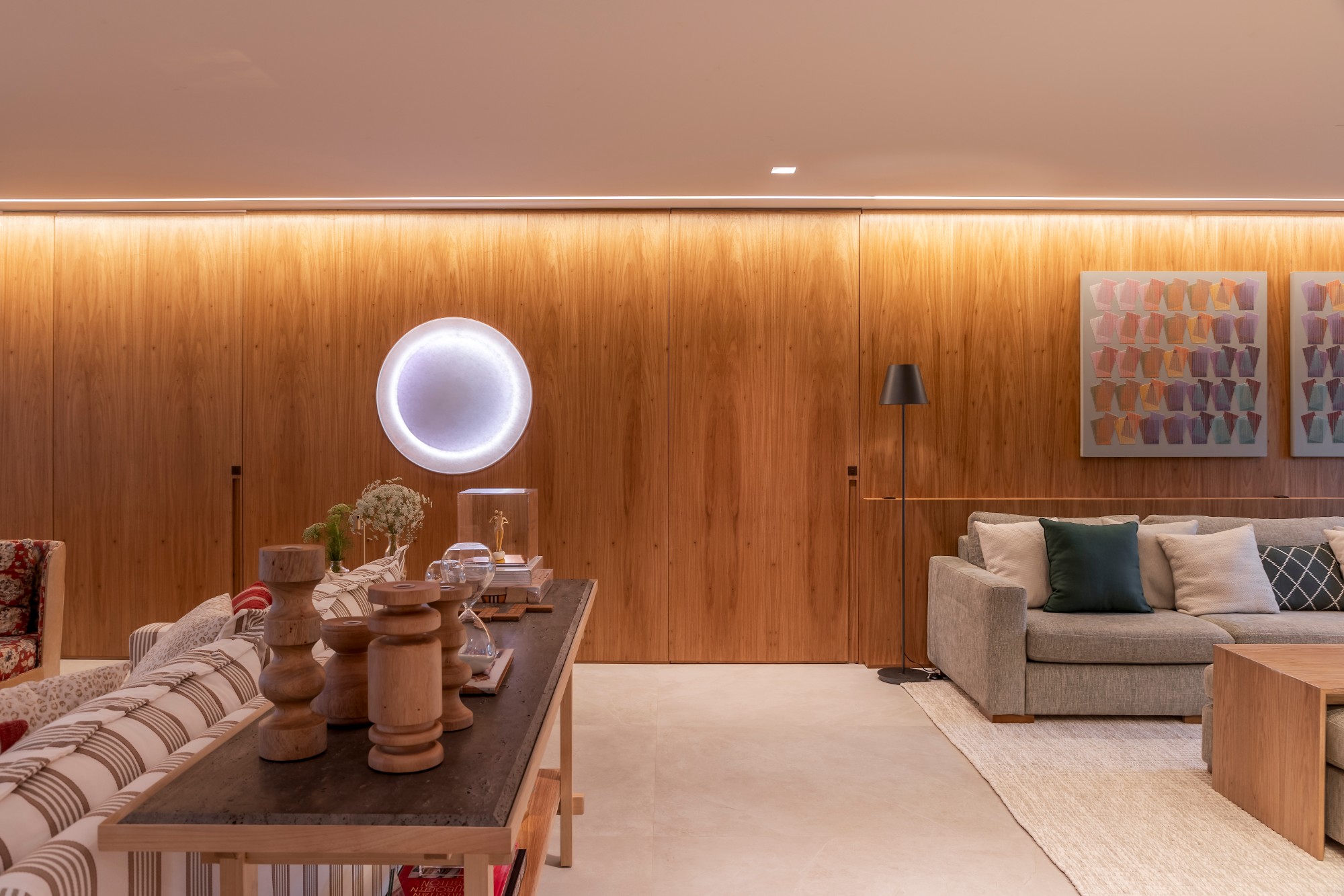 Living com painel de madeira, portas ocultas, luz embutida e luminária circular